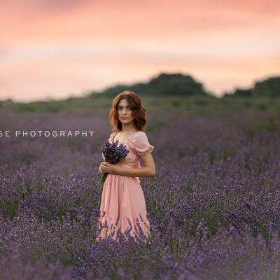 Teen girl in a pink dress holding lavender bouquet in a blooming lavender field at sunset near Fowlerville, Michigan, photographed by Mirage Photography.