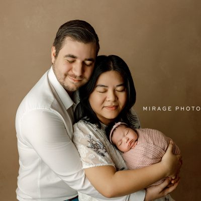 Mother and father holding their newborn baby in a cozy wrapped pose during a studio photography session in Fowlerville, Michigan by Mirage Photography