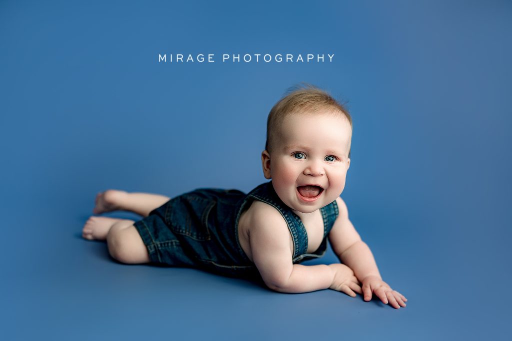 Smiling baby boy in denim romper during milestone photography session in Fowlerville, Michigan – Mirage Photography