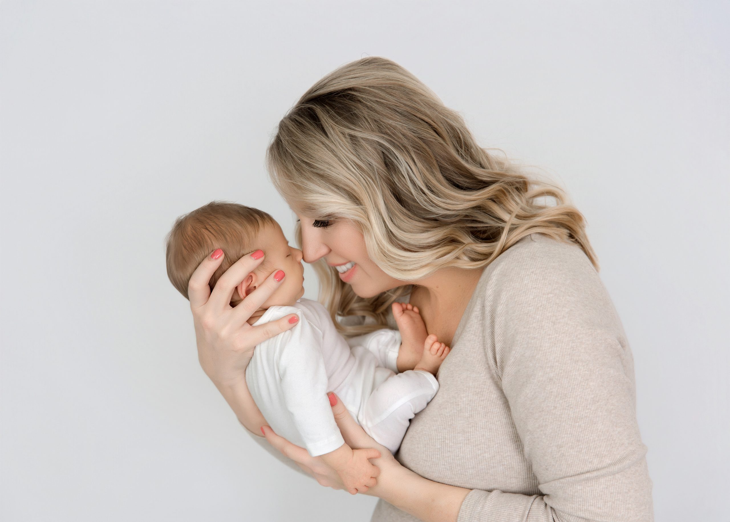 Mom in neutral outfit holding a newborn swaddled in a soft wrap.