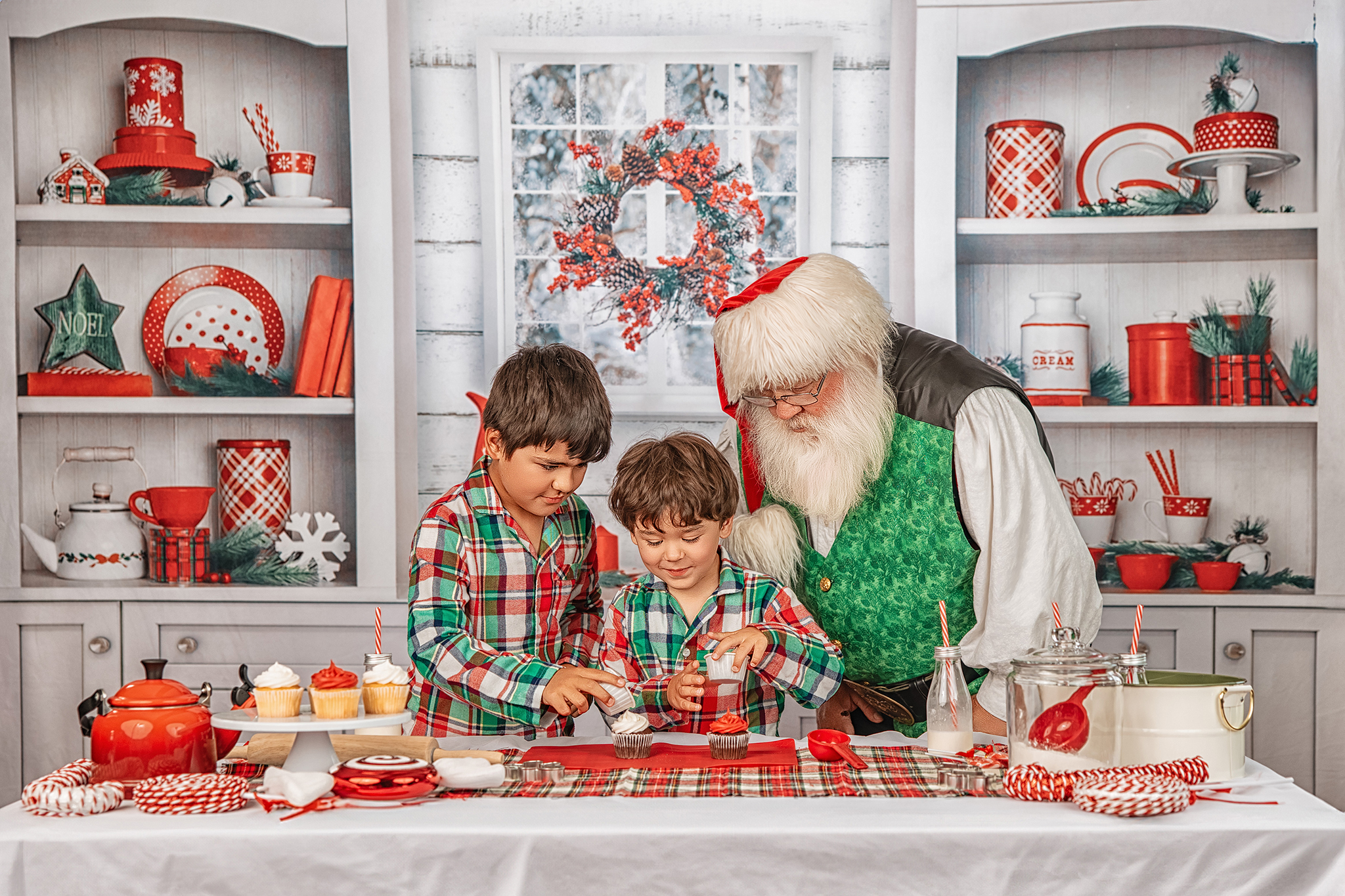 Santa helping two boys decorate cupcakes on a Christmas baking set