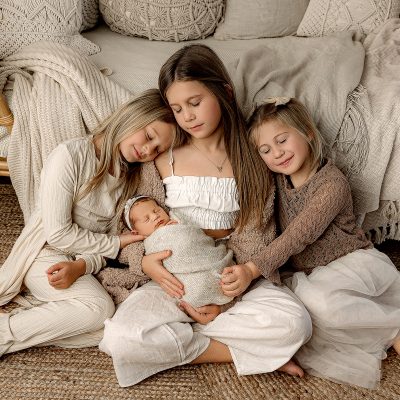 3 sister holding newborn baby in studio in fowlerville, mi