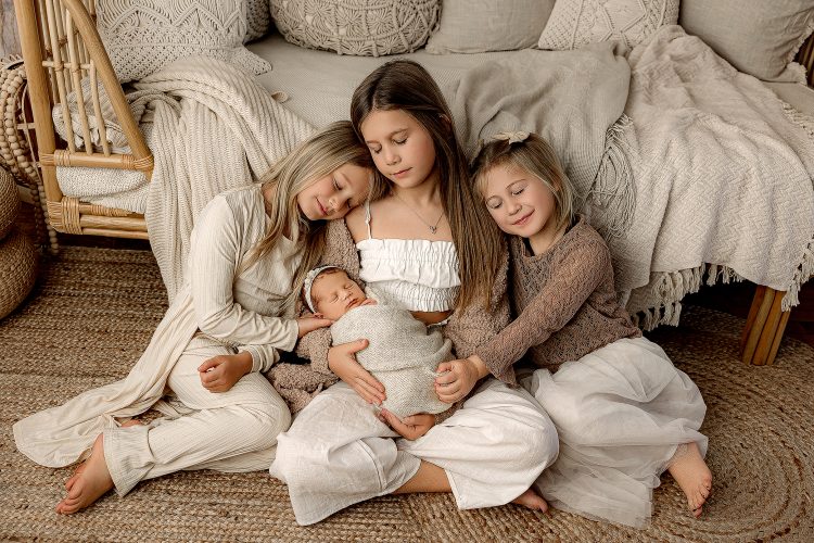 3 sister holding newborn baby in studio in fowlerville, mi